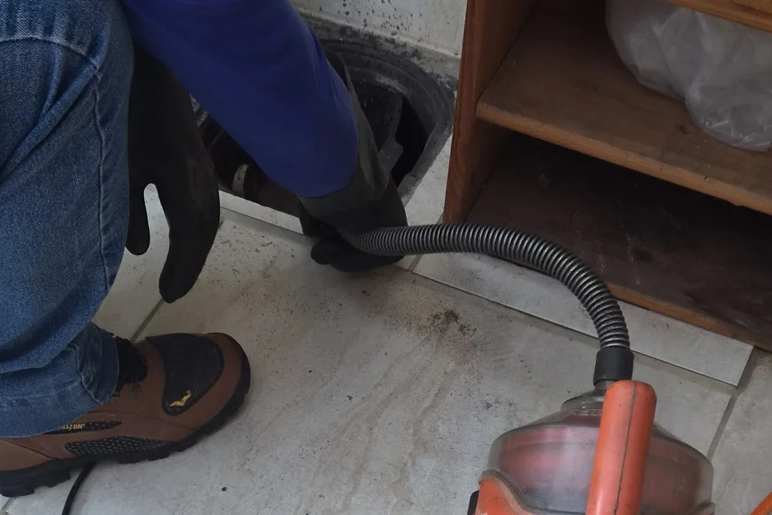 Técnico com luvas usando a máquina de cabo para desentupir uma tubulação