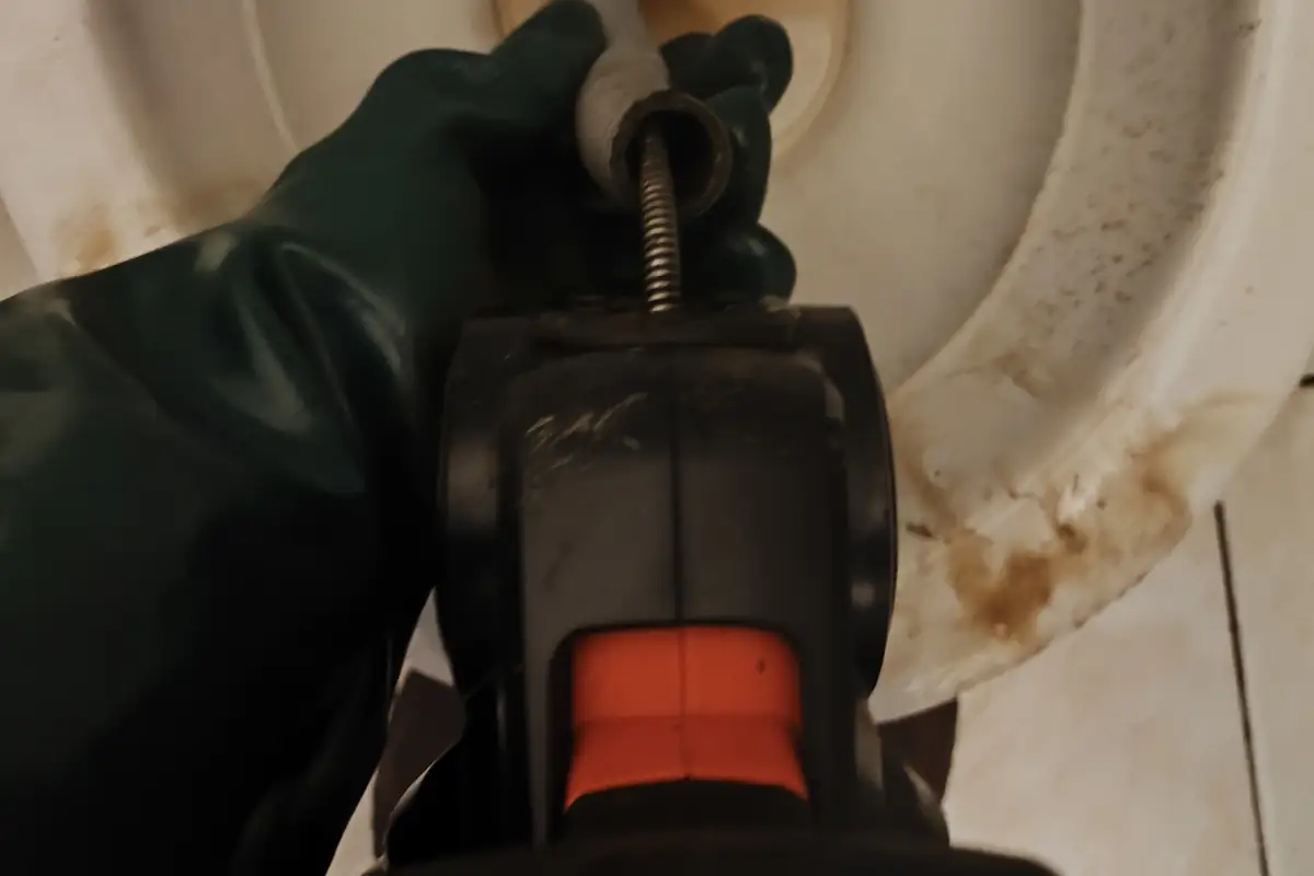 Máquina de desentupimento manual dentro do vaso sanitário, segurada por mão com luva